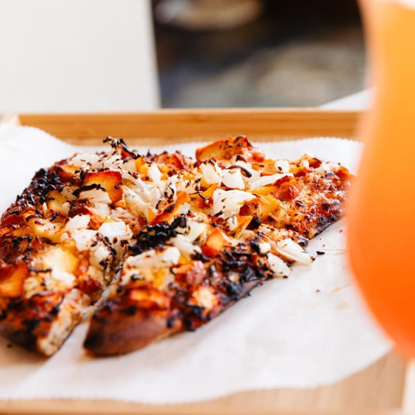 Two slices of Lemon Drop's bar-and-grill pizza with charred crust and white toppings on parchment paper.