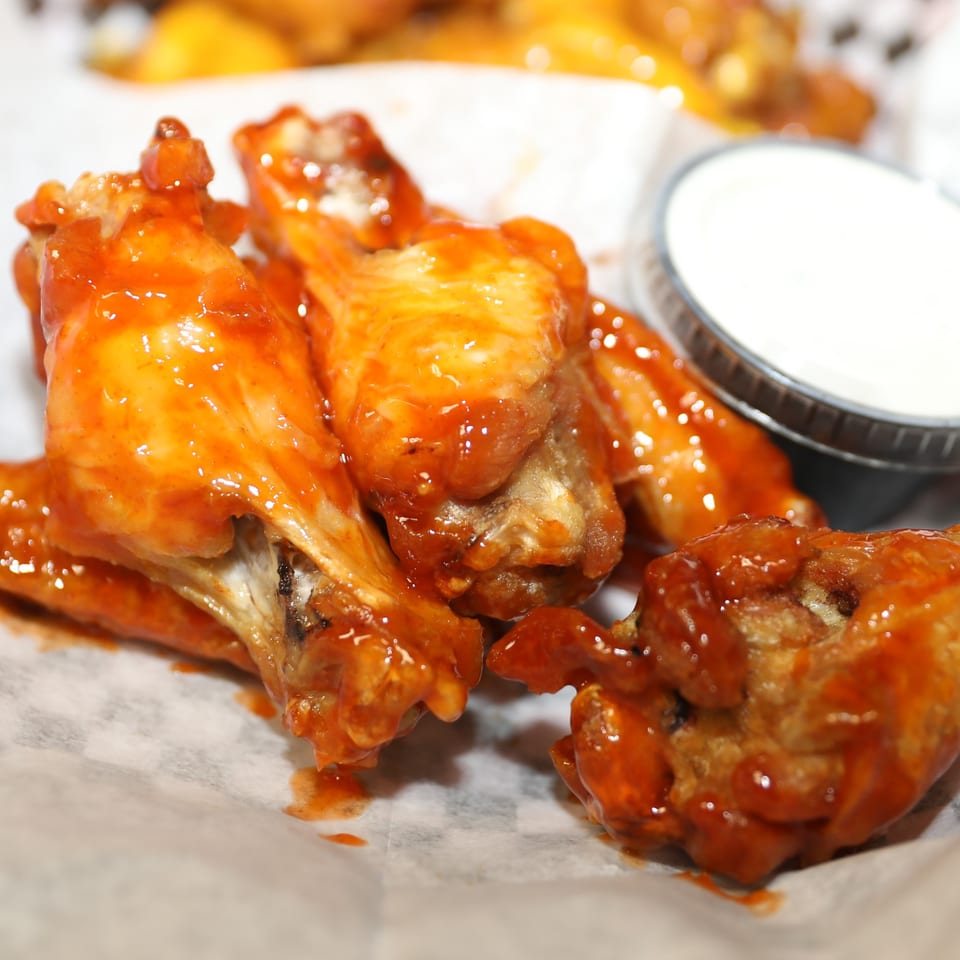 Close-up of several buffalo chicken wings with orange sauce and a side of ranch dressing.